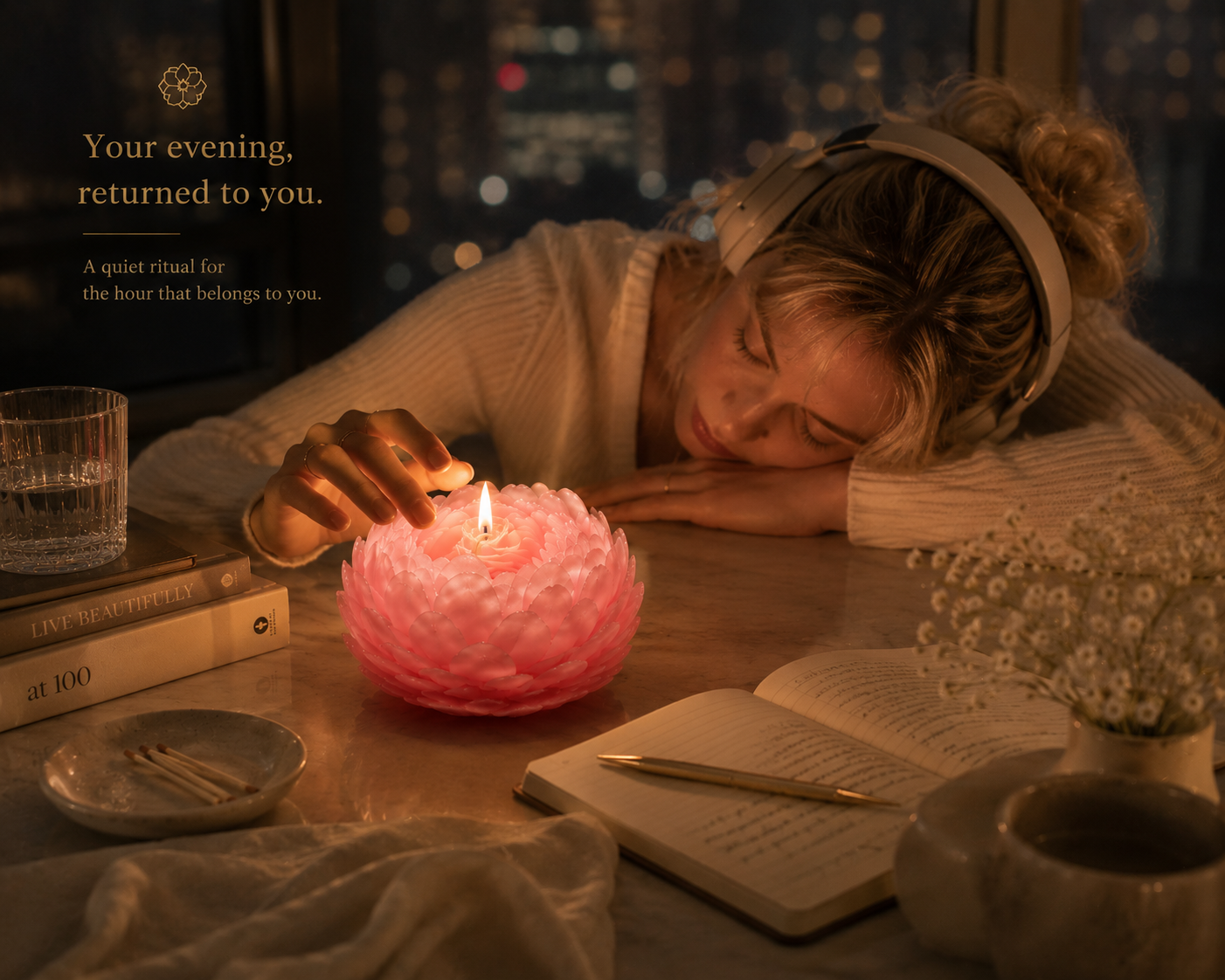 Woman wearing headphones beside a glowing Couture Peony Sculptural Candle on a desk at night, creating a quiet solo ritual with books, journal, and city lights.