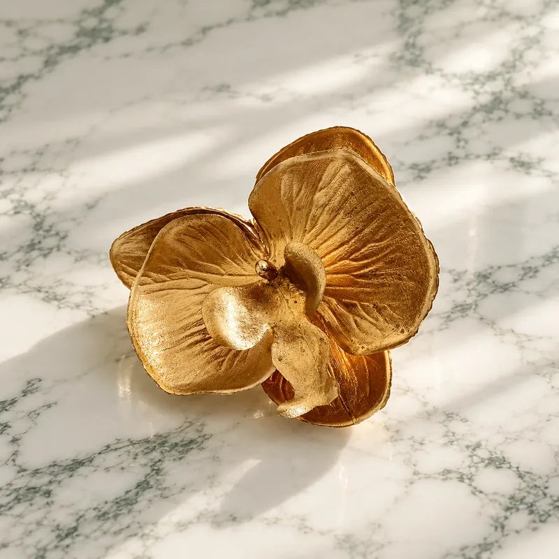 Gold orchid-shaped Founding Bloom object in warm window light.