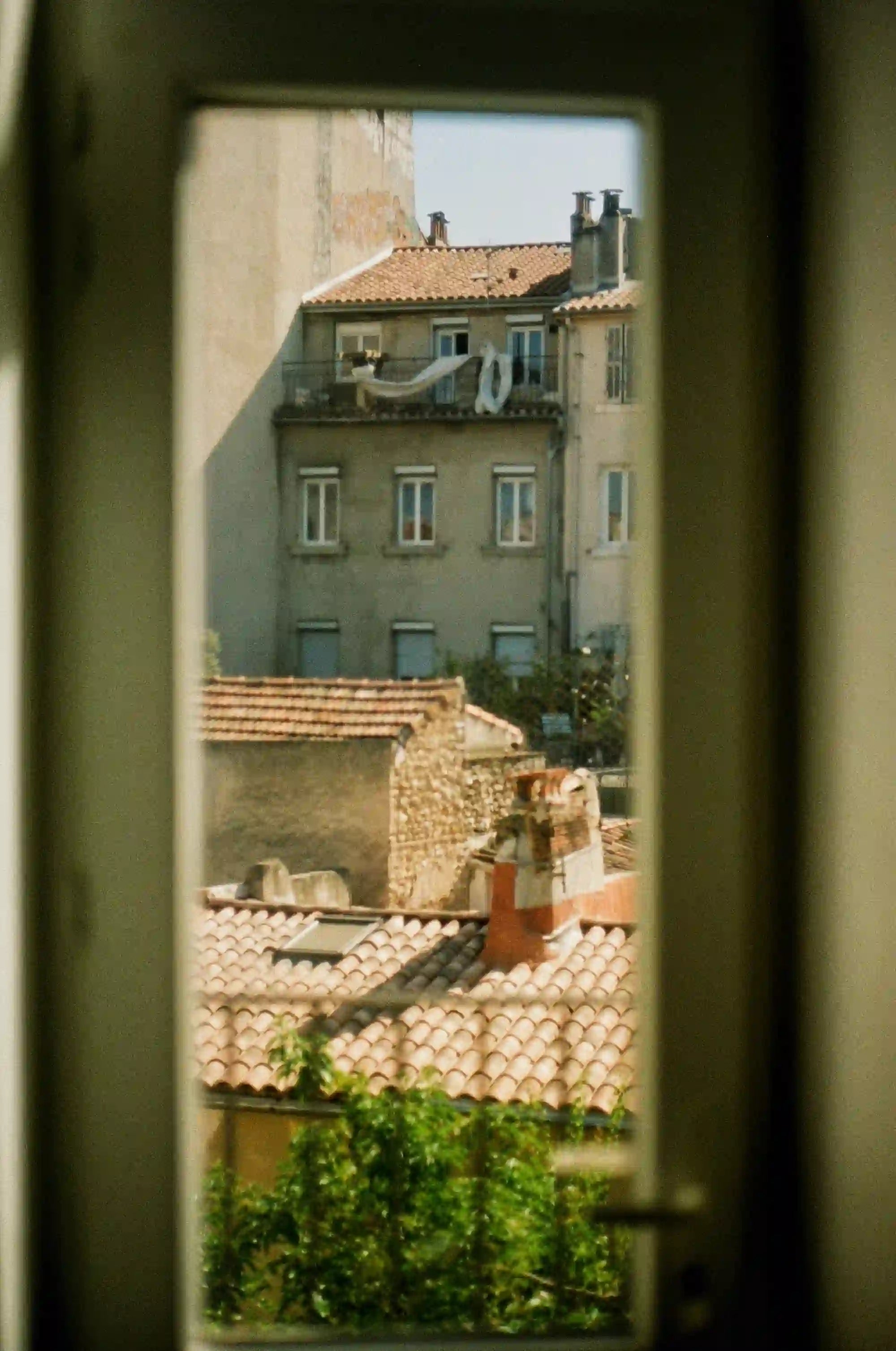 Looking out through an open window frame at sunlit European rooftops and a church tower.